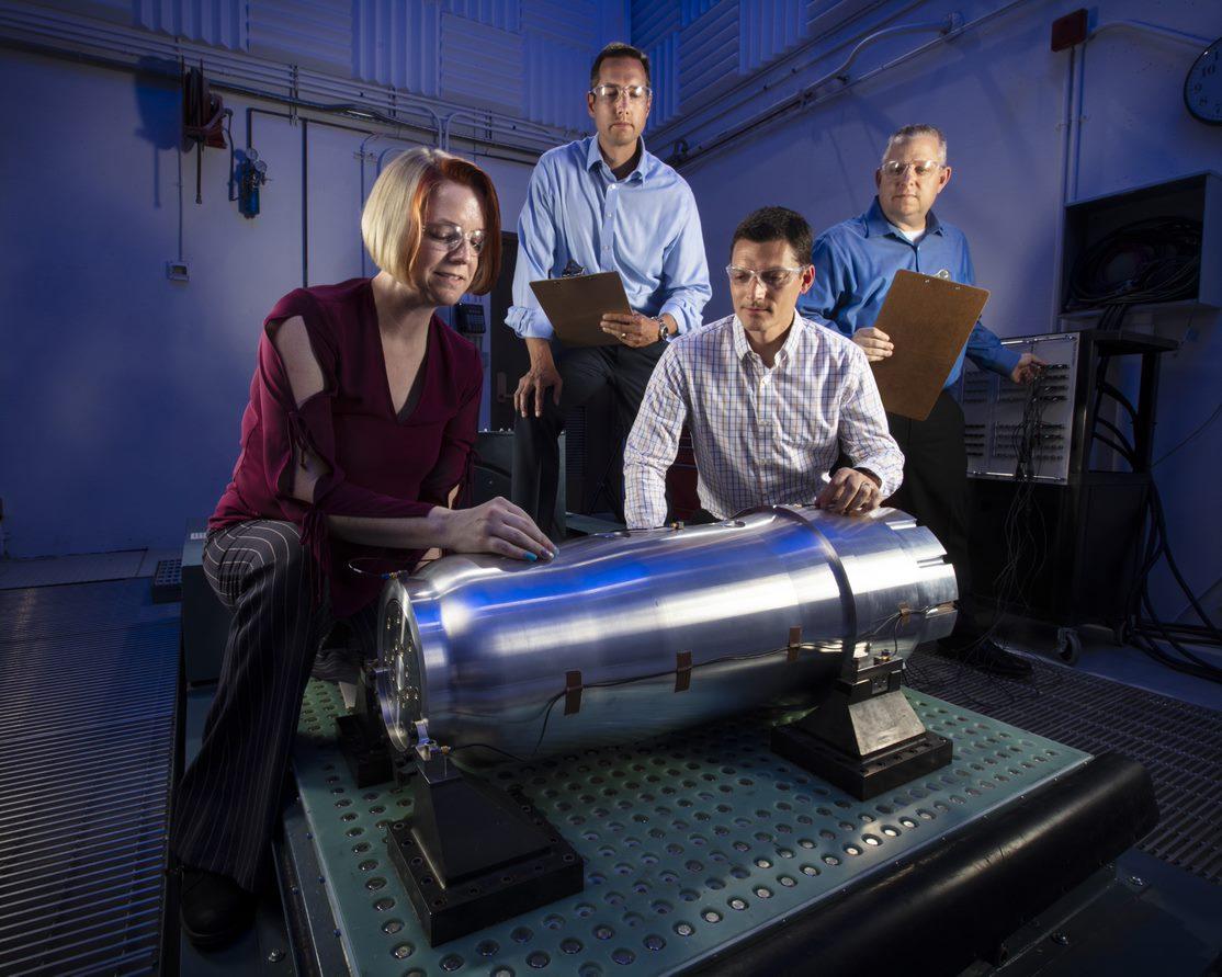 Four people working with cylindrical equipment.