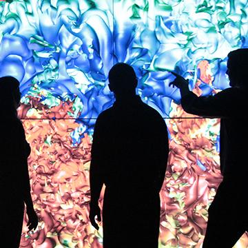 Computer scientists viewing models that appear as colored swirls on large screen in front of them