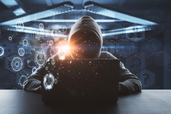 A hooded figure sitting with a laptop computer