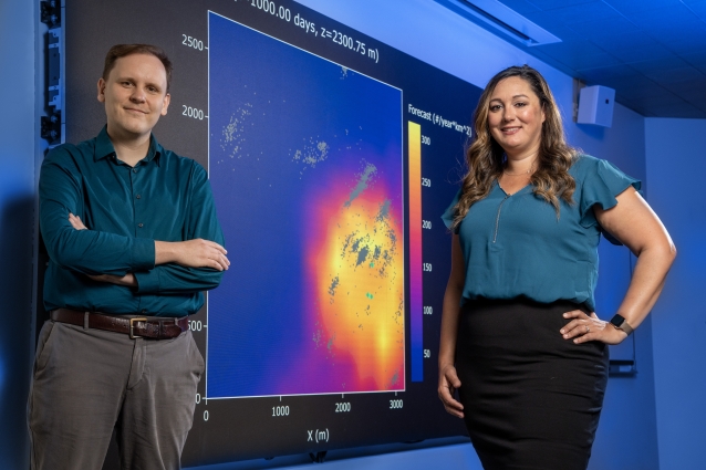 Two scientists stand before a screen displaying their research.